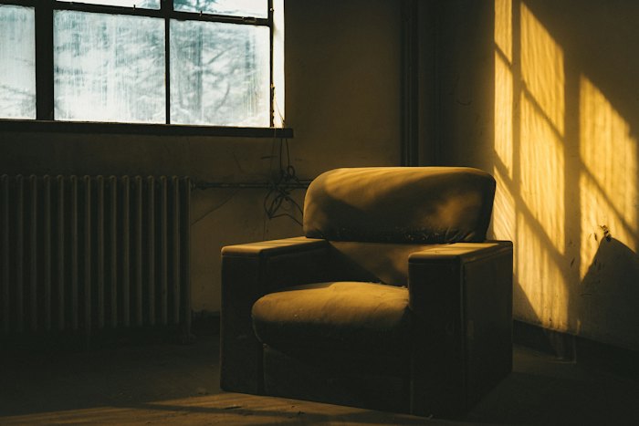 An armchair in a quiet room, warm sunlight falling through the window onto the wall.