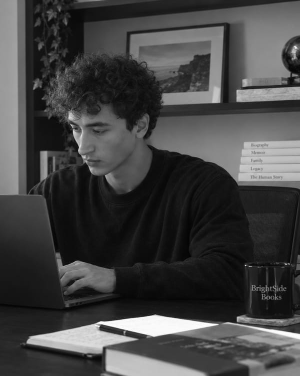 Alex Alickolli, the founder of BrightSide Books, typing on a laptop at a desk, with a BrightSide Books mug and an open notebook beside him.
