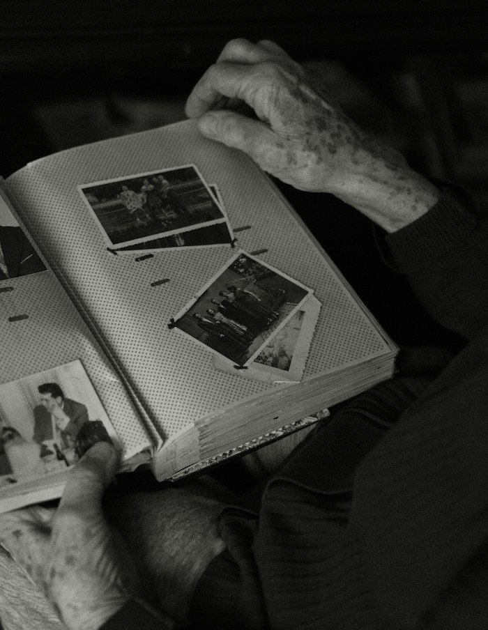An older person’s hands holding open a family album of black-and-white photographs.
