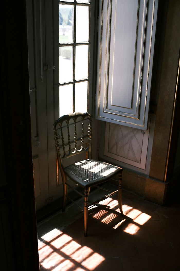 A wooden chair beside a tall open window, sunlight on the floor.