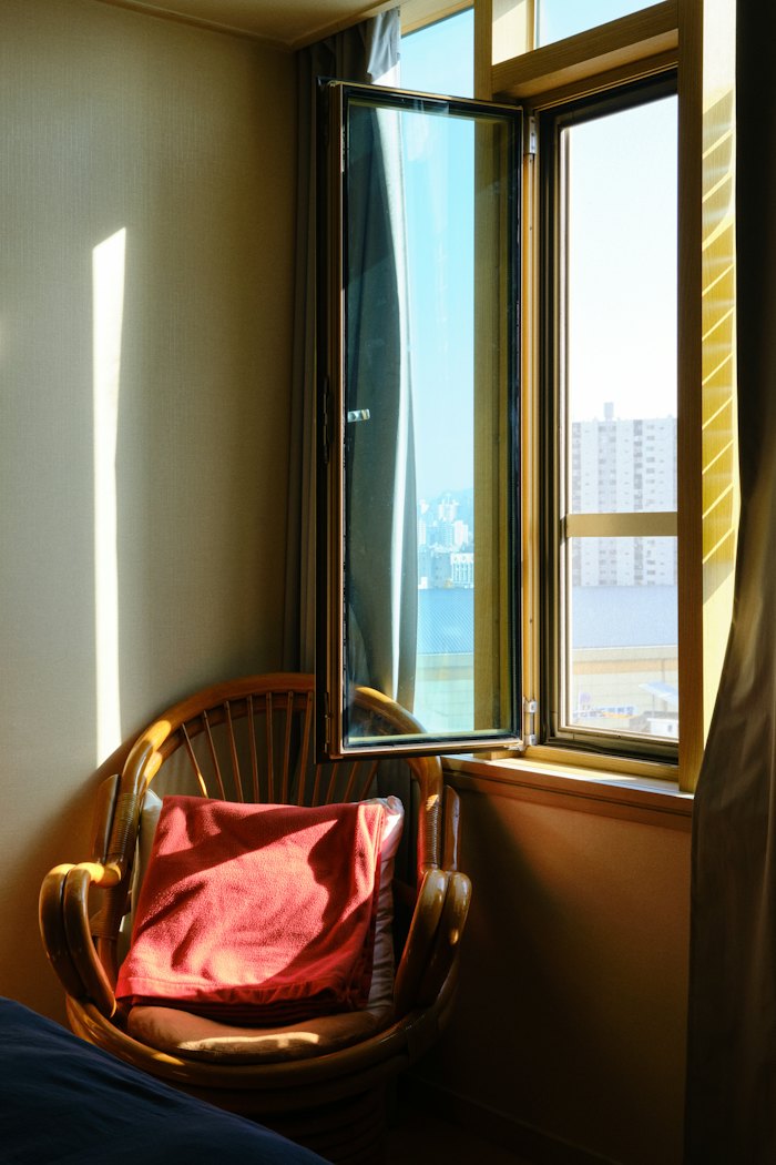 A wicker chair with a red cushion beside an open window in late sun.