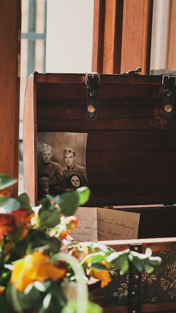 Old family photographs kept in a wooden chest beside a vase of flowers.