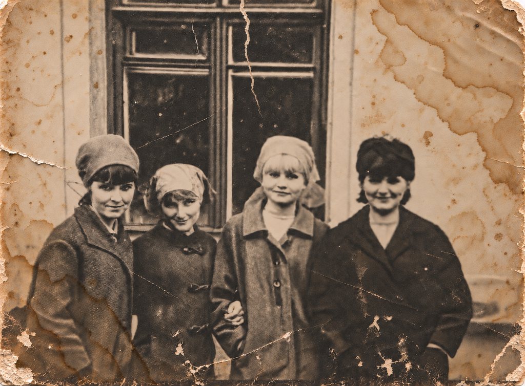 A damaged photograph of four women standing by a window, stained brown and cracked across the middle.